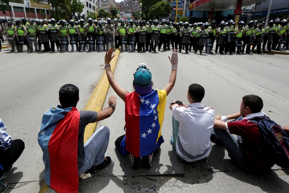 Участники шествия оппозиции сидят напротив бойцов национальной гвардии Венесуэлы.