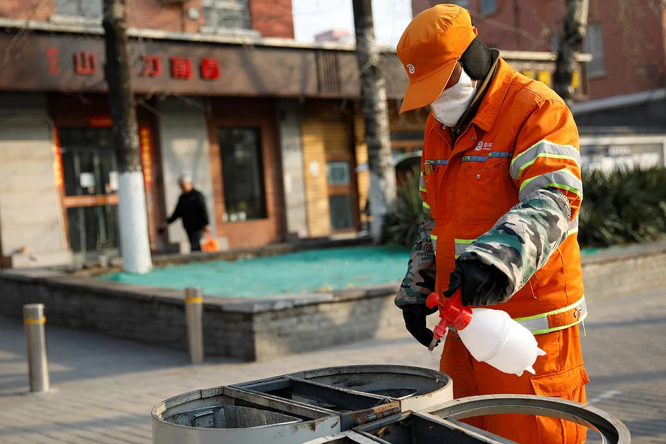 Дворник занят дезинфекцией мусорных контейнеров на опустевших улицах Пекина.
