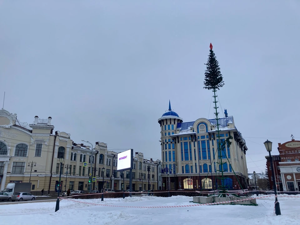 Пока что площадь вокруг ёлки огорожена специальной лентой, а рабочие завершили установку только верхних рядов праздничного дерева