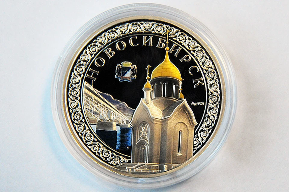 На реверсе монеты - герб города, мост через Обь и часовня в центре России.