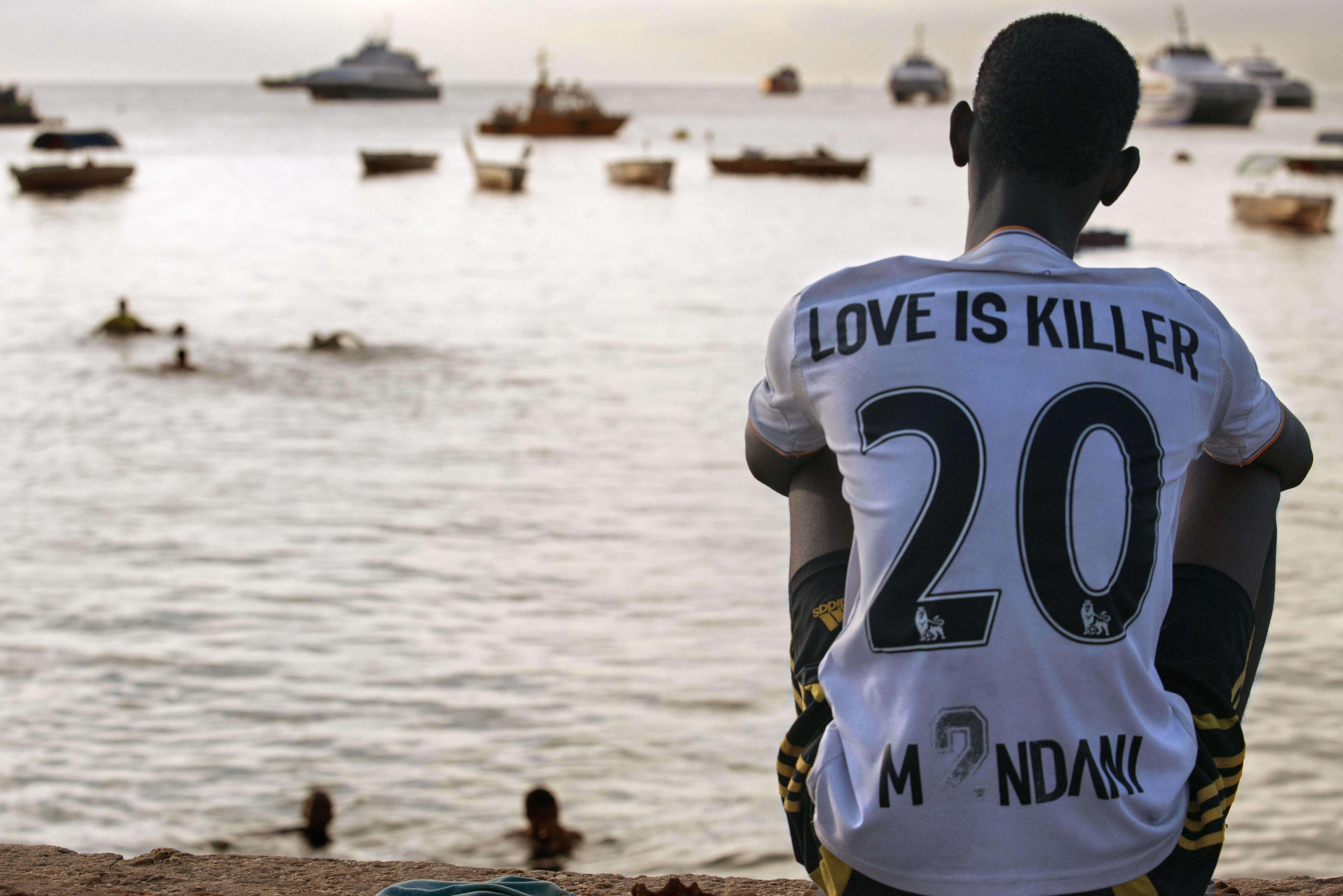 Мальчик наблюдает за лодками рыбаков у побережья Занзибара, Танзания.